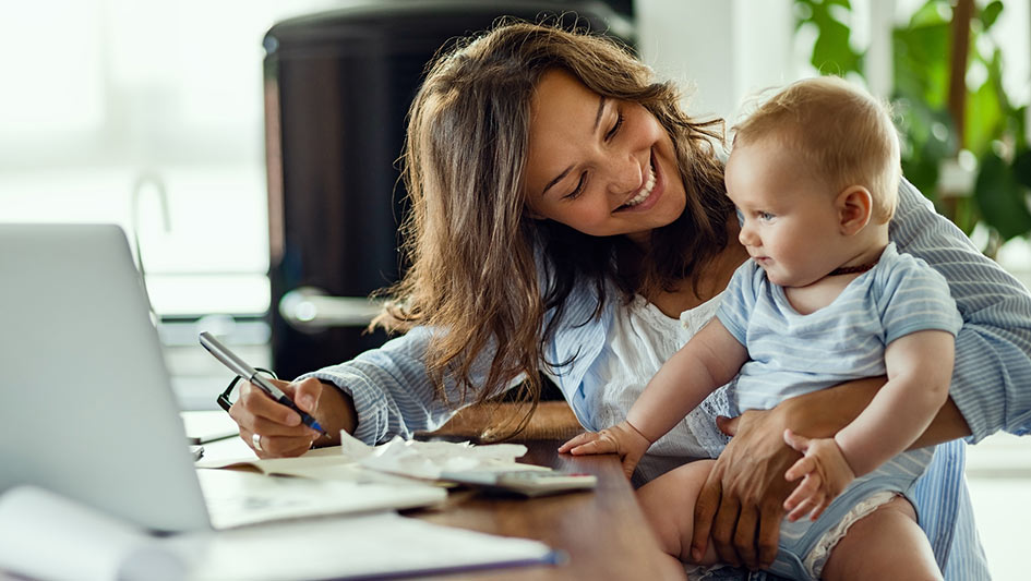 woman holding her baby while doing paperwork