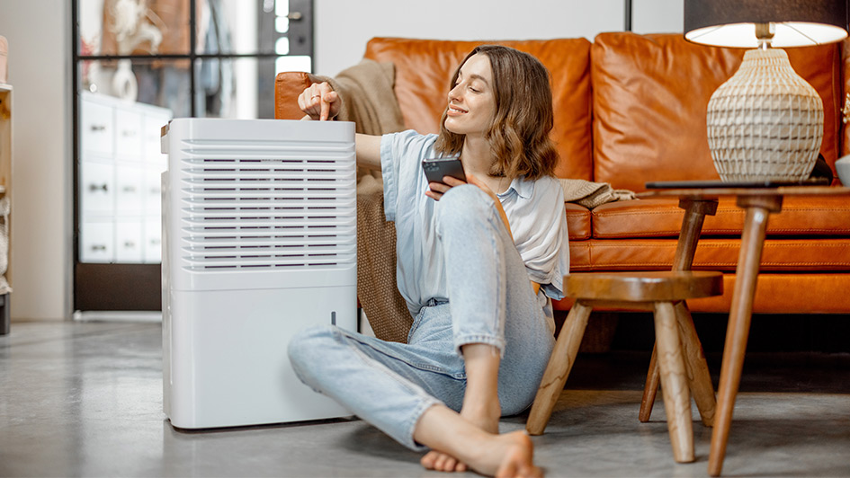Woman sitting next to a dehumidifier on her living room floor